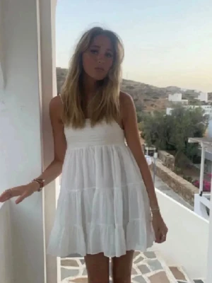 Vit kort sommarklänning med volanger - Säljer en vit kort klänning med volanger och ärmlös design. Klänningen har en luftig passform och tunna axelband, perfekt för varma dagar. Materialet ser ut att vara bomull och klänningen har en romantisk och enkel stil.