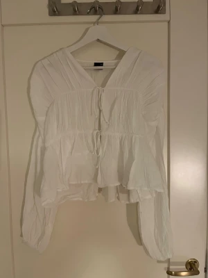 Vit blus med knytning - Luftig vit blus med v-ringning och knytning framtill från Gina Tricot. Blusen har långa ärmar och ett lätt rynkat tyg. Blusen är endast använd en gång. 