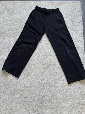 Svarta mjukisbyxor med raka ben - Svarta mjukisbyxor med bred resår i midjan och raka, lösa ben. Perfekta för chill eller träning. Materialet är mjukt och bekvämt, troligen bomull eller polyester. Diskret logga på framsidan.