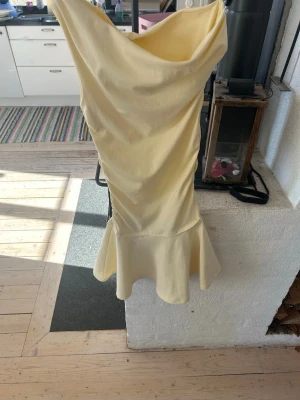 Ljusgul klänning från Zara - Supersnygg ljusgul klänning från Zara med draperad halsringning och volang nedtill. Klänningen har en figurnära passform och är tillverkad i ett mjukt material som känns bekvämt mot huden. Perfekt för dig som vill sticka ut med en fräsch och trendig look. Aldrig använd eftersom den var förliten. Nypris 400kr, sitter mer som en XS