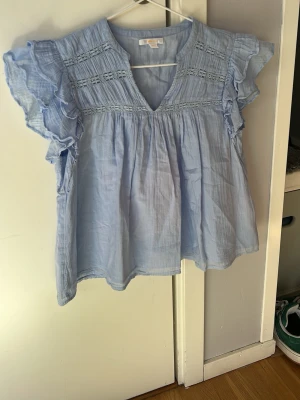 Ljusblå volangblus från Gina Tricot - Säljer en  ljusblå blus med volangdetaljer på ärmarna och spetsinslag upptill från Gina tricot💕💕 Blusen har en luftig passform, v-ringning och är tillverkad i ett tunt, mjukt tyg💕💕I mycket gott skick💕💕Nypris är 230 kr, jag säljer den för 75 kr💕💕Hör av er vid intresse 💕💕