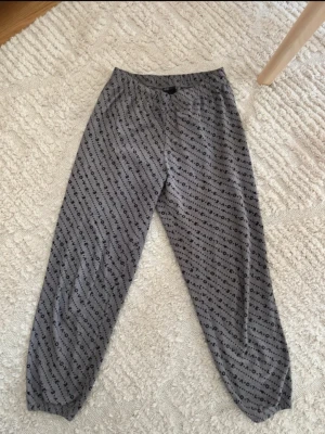 Grå mjuka loungewearbyxor H&M - Grå loungewearbyxor från H&M i supermjukt fleecematerial. Byxorna har ett svart diagonalt LOVE-mönster över hela tyget och resår i midjan samt vid bensluten. Perfekta för chill hemma eller mysiga kvällar.