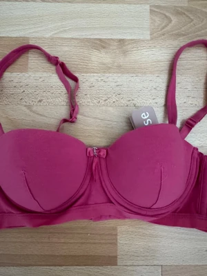 Ny. Mörkrosa bh. - Snygg mörkrosa  bh  med  bygel. Justerbara axelband och liten rosett framtill. Tillverkad i mjukt material för extra komfort.