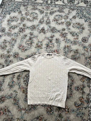 Vit/beige  kabelstickad tröja - Säljer en klassisk vit/beige kabelstickad tröja med rund hals och långa ärmar., vilket ger en snygg och tidlös look. passar 155-165 men står S