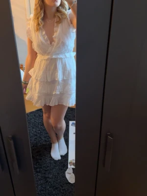 Vit studentklänning med volang - Supersöt vit kortklänning med  flera lager volanger. Klänningen har v-ringning, markerad midja och är ärmlös med volangdetaljer vid axlarna. Perfekt för er som tar studenten eller har avslutning. Jag beställde flera klänningar samtidigt och valde en annan så denna är helt ny med prislapp, endast testad!💕
