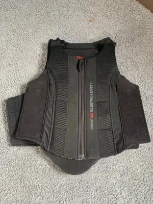 Ryggplatta från  Swing child XL - Säljer en svart säkerhetsväst från Swing i storlek child XS, perfekt för ridning. Ryggplattan har dragkedja framtill, breda kardborreband i sidorna. Säljer då den e för stor för mig💕