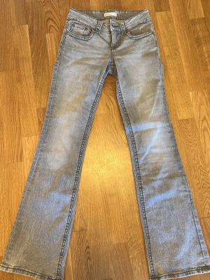Ljusblå bootcut jeans från Lee - Säljer ett par ljusgrå bootcut jeans från Gina tricot. Jeansen har låg midja och är tillverkade i mjuk denim. Bakfickorna har lock och knappdetaljer för extra stilpoäng. Perfekta för en avslappnad look.