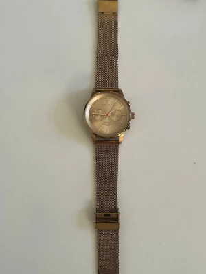 Guldfärgad Triwa Nevil mesh-klocka - Stilren klocka från Triwa, modell Nevil, med guldfärgat mesh-armband och matchande urtavla. Klockan har kronograf-funktion och tydliga indexmarkeringar. Perfekt accessoar för dig som gillar en clean och modern look.