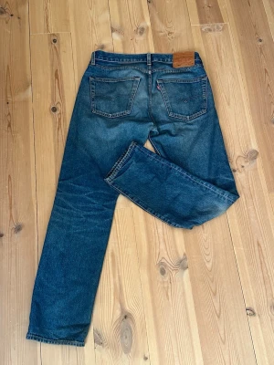Levi's blå raka jeans - Klassiska blå jeans från Levi's med rak passform. Jeansen har tydliga sömmar och den ikoniska läderlappen bak i midjan. Tillverkade i slitstark denim, perfekta för en avslappnad och tidlös stil.
