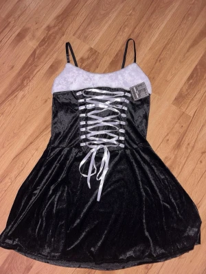 Svart julklänning med korsettliknande snörning - Helt ny svart kortklänning från Heavy X-MAS med fluffig vit kant upptill och smala axelband. Framsidan har snygg snörning med vita band. Perfekt för julens. Står storlek L/XL men passar M