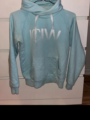Ljusblå hoodie från ICANIWILL - Mysig ljusblå hoodie från ICANIWILL med stor ficka framtill och vit logga på bröstet. Huvan har vita snören och tröjan är tillverkad i mjuk bomullsmix. Perfekt för chill dagar eller till träningen.
