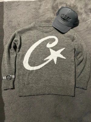 Grå stickad tröja med stjärnmotiv - Cool grå stickad tröja med stort vitt C och stjärna på framsidan. Tröjan har rund halsringning och långa ärmar. Perfekt för dig som gillar grafiska mönster och vill ha något som sticker ut i garderoben.