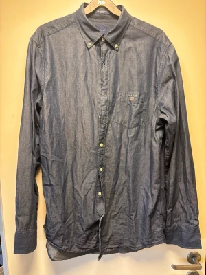 Mörkblå skjorta från Gant - Klassisk mörkblå skjorta från Gant i bomull med knappslå och bröstficka med broderad logga. Skjortan har lång ärm, button down-krage och vita knappar. Perfekt till jeans eller chinos för en clean och stilren look.