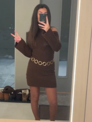 Brun ribbad offshoulder klänning - Säljer en brun kort ribbad klänning med offshoulder-design och långa ärmar. Med  Klänningen så får man en snygg guldfärgad kedja i midjan som detalj. Köpte den utan bältet men säljer den med bältet. Perfekt för dig som vill ha en trendig och bekväm look.
