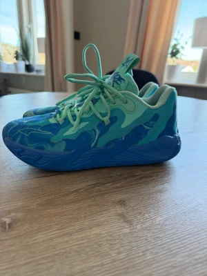 Blå-turkosa sneakers med mönster - Säljer ett par riktigt snygga basket skor i blått och turkost med coola mönster på sulan och ovandelen. Skorna har mesh och syntetmaterial för bra andningsförmåga och komfort. Perfekta för dig som vill sticka ut med färg och stil på träningen. 