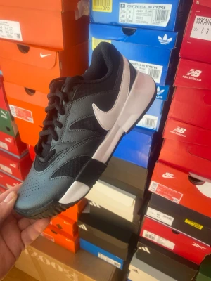 Nike Claybreaker Svart Vit - Snygga svarta Nike sneakers med vit sula och vit swoosh på sidan. Skorna har en låg profil och är tillverkade i en mix av läder och mesh för bra andningsförmåga. Perfekta för dig som gillar sportig och clean stil.