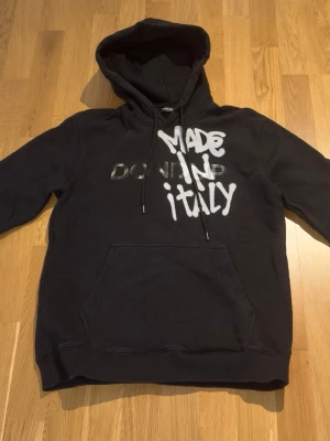 Svart hoodie från Dondup - Säljer en svart hoodie från Dondup, tillverkad i Italien. Hoodien har klassisk huva och ribbade muddar vid ärmslut och nederkant. Materialet är mjukt och bekvämt, perfekt för en avslappnad stil. Passar dig som gillar stilrena och tidlösa plagg. Ny pris ca 3000kr väldigt svår att hitta ny. 