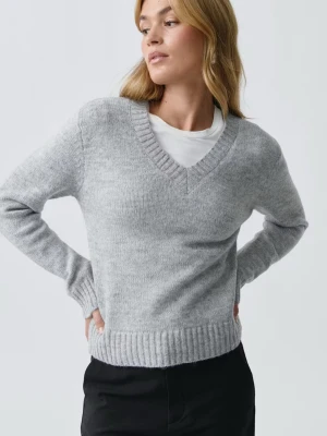 Ljusgrå stickad tröja med v-ringning - Mysig ljusgrå stickad tröja med v-ringad hals och ribbade muddar vid ärmslut och nederkant. Tröjan har en enkel, klassisk design och är perfekt att bära över en t-shirt. Materialet ser mjukt och bekvämt ut, och modellen är rak och avslappnad.