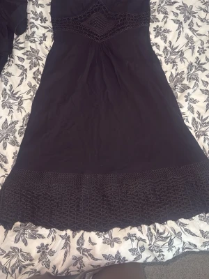 Svart klänning med spetsdetaljer - Snygg svart klänning med dekorativa spetsdetaljer vid midjan och nederkanten. Klänningen har en figurnära passform och är knälång. Perfekt för dig som gillar stilrena plagg med unika detaljer.