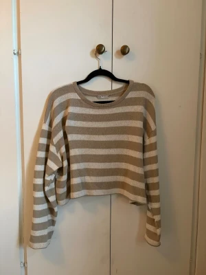Beige och vit randig stickad tröja - Säljer en beige och vit randig stickad tröja från Zara. Mjuk tunnare tröja med rund halsringning och långa ärmar. Perfekt för lager på lager eller för kallare sommardagar.