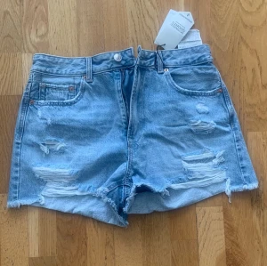 Ljusblå destroyed jeansshorts Stradivarius  - Säljer ett par ljusblå jeansshorts från stradivarius med slitna detaljer och råa kanter. Shortsen har fem fickor, bälteshällor och knappgylf. Perfekta för sommaren och ger en avslappnad vibe.