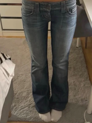 Blå bootcut jeans från Guess - Säljer ett par blå bootcut jeans från Guess med klassisk femficksdesign och snygga slitningar. Jeansen har låg midja och subtila detaljer på bakfickorna. Perfekta för en avslappnad och trendig look. Midjemåttet är 37 cm och innerbenslängden är 80. Jag är 167❤️❤️