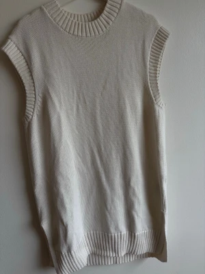 Ljus stickad väst med ribbade detaljer - Säljer en ljus stickad väst med breda ribbade kanter vid hals, ärm och nederkant den har även slit på båda sidorna. Västen har en enkel och clean design utan mönster, perfekt att styla över en skjorta eller t-shirt. 🌸