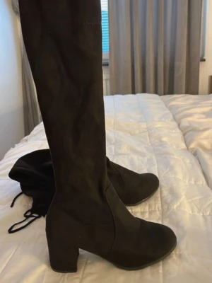 Svarta overknee stövlar med klack - Säljer ett par svarta overknee stövlar i mockaimitation med bred klack och rund tå. Stövlarna har en stilren design och går högt upp på benet. Perfekta till höstens och vinterns outfits.