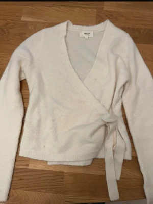 Vit omlottkofta med knytband - Mysig vit omlottkofta med långa ärmar och knytband i midjan. Koftan har en djup V-ringning och är tillverkad i ett mjukt, fluffigt material som känns skönt mot huden. Perfekt för lager på lager och enkel att styla till olika outfits. Koftan är från Gina, storlek s. Koftan säljs inte längre🥰