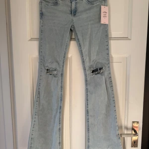 Ljusblå bootcut jeans med slitningar - Säljer ett par jättefina ljusblå jeans i bootcut-modell. Trendiga slitningar vid knäna och snygga rosa detaljer på bakfickorna.  ✨ Helt oanvända (lappen kvar) ✨ Stretchigt och skönt material