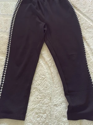 Svarta leggings från SHEIN med mönstrade sidor - Säljer ett par svarta leggings från SHEIN i storlek L. De har elastisk midja och coola svartvita hundtandsmönstrade ränder längs sidorna. Materialet är stretchigt och bekvämt, perfekt för en chill och trendig look.