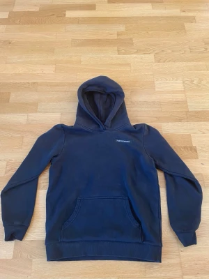 Svart hoodie från Peak Performance - Snygg svart hoodie från Peak Performance med klassisk huva och magficka. Diskret logga på bröstet och mjukt, fleecefodrat material på insidan som gör den extra skön. Perfekt för chill dagar eller när du vill ha en enkel men stilren look.