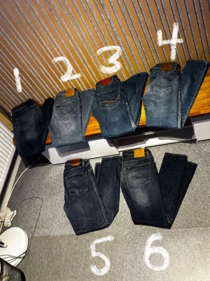 Mörkblå raka jeans med läderpatch - Säljer flera par mörkblå och mellanblå jeans med raka ben och klassisk femficksdesign. Alla har en brun läderpatch bak i midjan och kontrastsömmar. Perfekta för en avslappnad och stilren look. Materialet är denim i bomull.  Säljes i både bulk med rabatterade priser. Samt styck 250kr priset är diskuterbart