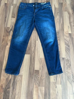 Blå jeans från replay - Säljer ett par klassiska blå jeans från replay med raka ben och fem fickor. Jeansen har en mörk tvätt med lätt slitning på framsidan och detaljerade sömmar på bakfickorna. Perfekta för en avslappnad och stilren look.
