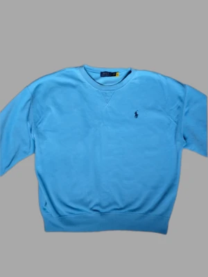 Ljusblå sweatshirt från Polo Ralph Lauren - Snygg ljusblå sweatshirt från Polo Ralph Lauren med klassisk rund halsringning och broderad logga på bröstet. Tröjan har ribbade muddar vid ärmslut och nederkant. Perfekt för en avslappnad och stilren look.