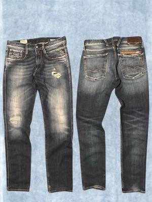 Replay Anbass (Vintage med slitningar) - Säljer ett par mörkblå jeans från Replay  med slitningar och hål på låret och knät. Jeansen har klassisk femficksmodell, kontrastsömmar och en snygg tvättad look. Perfekta för dig som gillar en avslappnad och trendig stil.