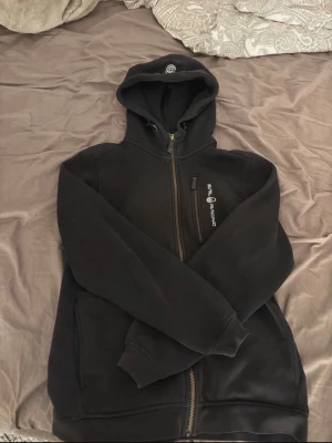 Svart hoodie från Sail Racing - Svart hoodie från Sail Racing med dragkedja framtill och en extra bröstficka med dragkedja. Den är använd några gånger, ser använd ut. storlek 160. 