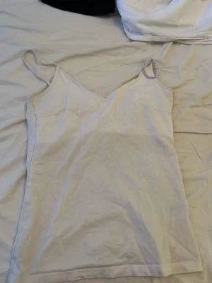 Vit linnetopp med smala axelband - Snygg vit linnetopp med smala axelband och v-ringad hals. Enkel och stilren design som passar perfekt till jeans eller kjol. Tillverkad i mjukt bomullsmaterial för en bekväm känsla hela dagen.