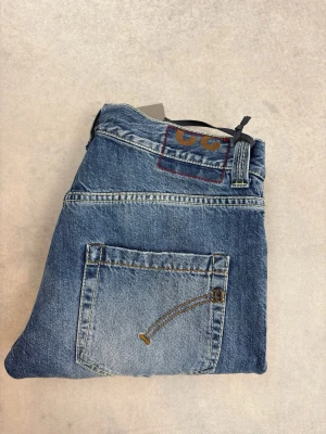 Blå slitna Dondup jeans med broderad ficka - Snygga blå jeans med slitningar på benen och en unik broderad bakficka. Jeansen har klassisk femficksdesign och raka ben. Perfekta för en avslappnad och trendig look.
