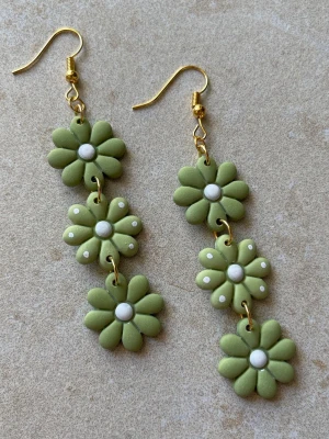 Handgjorda statementörhängen i grönt – blomdesign - Handgjorda statementörhängen i polymerlera  Varje blomma är formad för hand vilket gör att varje par är unikt och kan variera något i detaljer.  Ca 8 cm långa – tydliga men fortfarande lätta att bära.  Antiallergiska detaljer Lätta trots storleken Guldfärgade detaljer Flera par finns  Skriv om du vill se exakt par innan köp  Skickas
