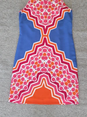 Färgglad kort klänning med grafiskt mönster - Snygg kort klänning med grafiskt mönster i blått, orange, rosa och vitt. Klänningen har ärmlös design och figurnära passform. Perfekt för dig som gillar färg och unika prints. 
