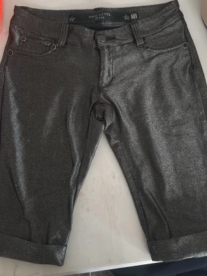 Metallicgrå jeans från High Level - Säljer ett par metallicgrå jeans från High Level Jeans. De har klassisk femficksdesign, uppvikta benslut och en snygg glansig finish som sticker ut. Perfekta för dig som vill ha något annorlunda i garderoben!