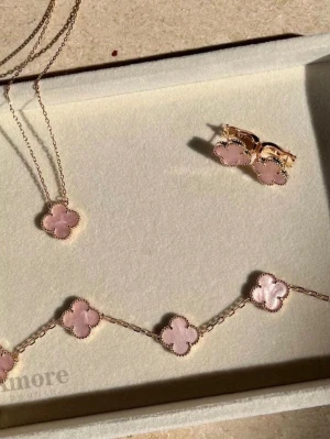 Smyckesset med rosa fyrklöver - Snyggt smyckesset med halsband, armband och örhängen i guldtonad metall med rosa fyrklöverformade hängen. Perfekt för dig som gillar unika och trendiga accessoarer med en feminin touch. Kedjorna är tunna och detaljerade, och klöverhänget har en fin pärlkant. Tillkommer även en ring. Boxen följer inte med. 