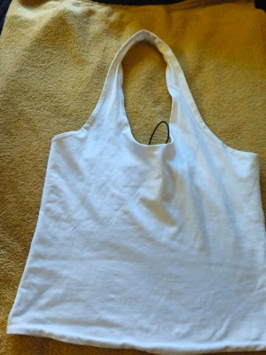 Vit linnetopp från Gina Tricot - Snygg vit linnetopp från Gina Tricot med djup urringning och breda axelband. Perfekt för varma dagar och enkel att matcha med jeans eller kjol. Tillverkad i mjuk bomull som känns skön mot huden.