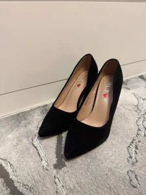 Svarta spetsiga pumps med klack - Snygga svarta pumps med spetsig tå och hög klack från I Love. Skorna har en klassisk siluett och är klädda i mockaliknande material med beige innersula. Perfekta för att lyfta vilken outfit som helst.