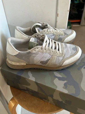 Valentino rockrunners - Snygga sneakers från Valentino i grått och beige camomönster. Skorna har meshpaneler, mockadetaljer och vita partier vid häl och snörning. Klassisk låg modell med robust sula och cool design. Perfekta för dig som gillar streetstyle och exklusiva märken. Box och dustbag ingår!
