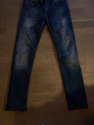 Blå slim fit jeans från J.Lindeberg - Snygga blå slim fit jeans från J.Lindeberg med klassisk femficksmodell och slitna detaljer. Jeansen har en något tvättad look och är tillverkade i denim med en skön passform. Perfekta för dig som gillar en stilren och modern look. Storlek 31/32