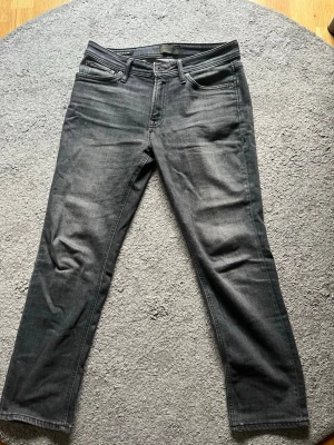 Mörkgrå jeans från Jack & Jones - Snygga mörkgrå jeans från Jack & Jones i modellen Regular Clark. Klassisk femficksdesign med dragkedjegylf och raka ben. Perfekta för en avslappnad och stilren look. 31/30 i storlek