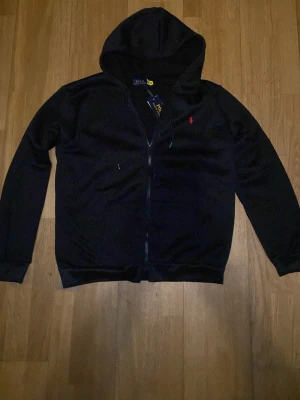 Svart ziphoodie Polo Ralph Lauren - Svart hoodie med dragkedja från Polo Ralph Lauren. Med röd loga i storlek S men passar även M