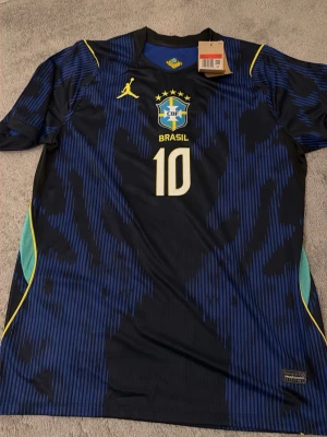 Blå Brasilien fotbollströja nr 10 - Snygg blå Brasilien fotbollströja från Jordan med nummer 10 på bröstet. Tröjan har gula detaljer, CBF-emblem och stjärnor ovanför loggan. Tillverkad i lätt och ventilerande material, perfekt för träning eller match.